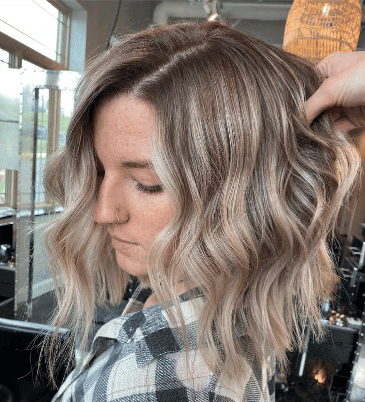 Woman with wavy, shoulder-length blonde hair styled in a modern salon.