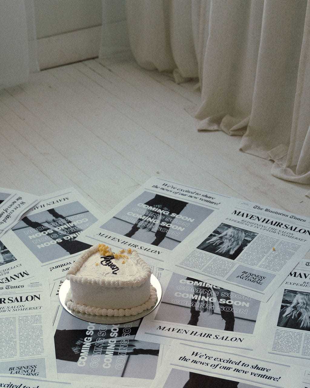 Cake on a floor surrounded by newspaper pages announcing the opening of Maven Hair Salon.