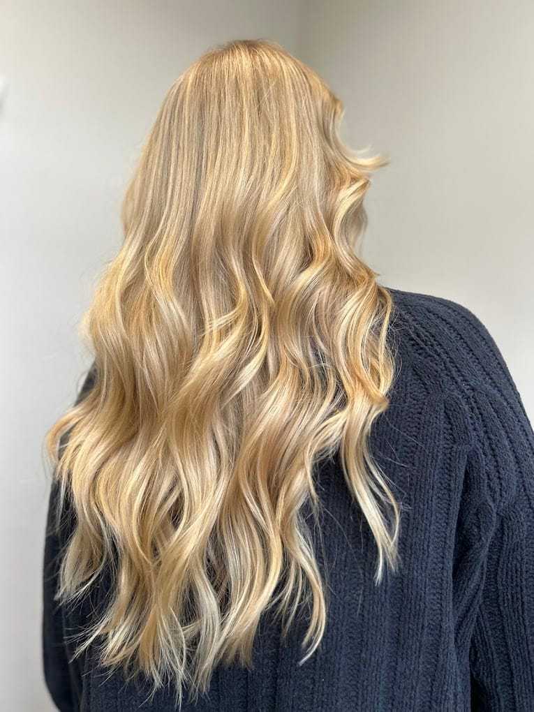 Blonde hair with loose waves cascading down the back of a person wearing a dark sweater.